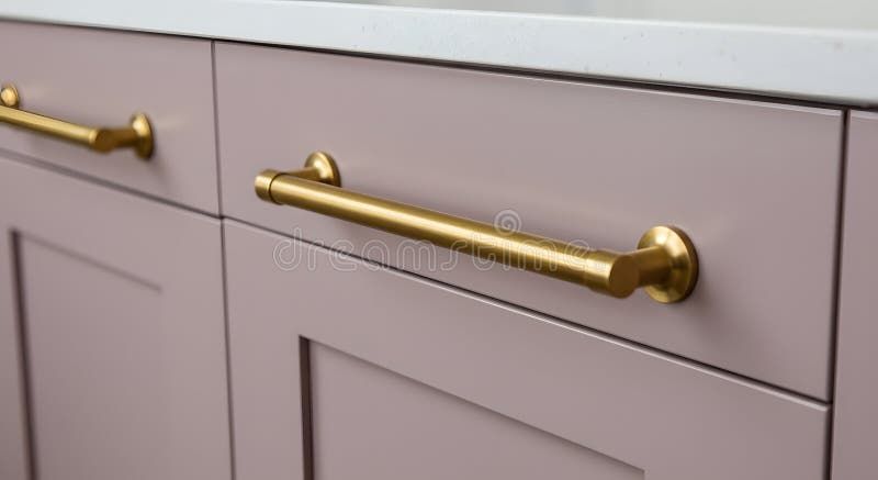 Moderne goldene Möbelgriffe auf altrosa Küchenschubladen.
